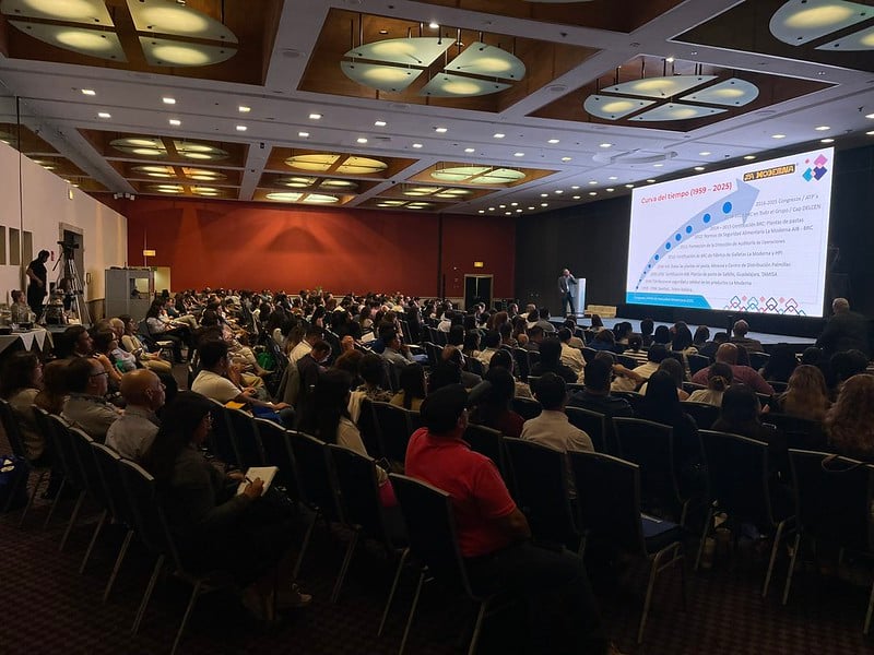 Auditorio del Congreso Latam de Inocuidad Alimentaria durante una ponencia con la curva del tiempo de La Moderna en pantalla